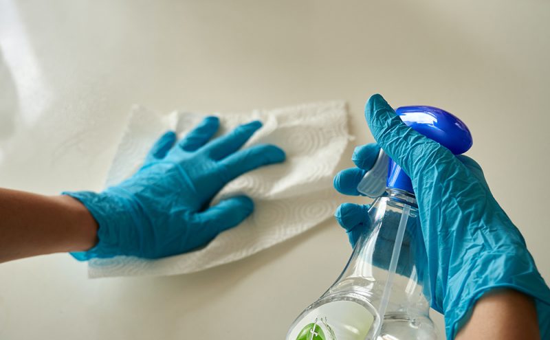 Two hands wearing cleaning cloves and holding a cloth and a cleaning spray